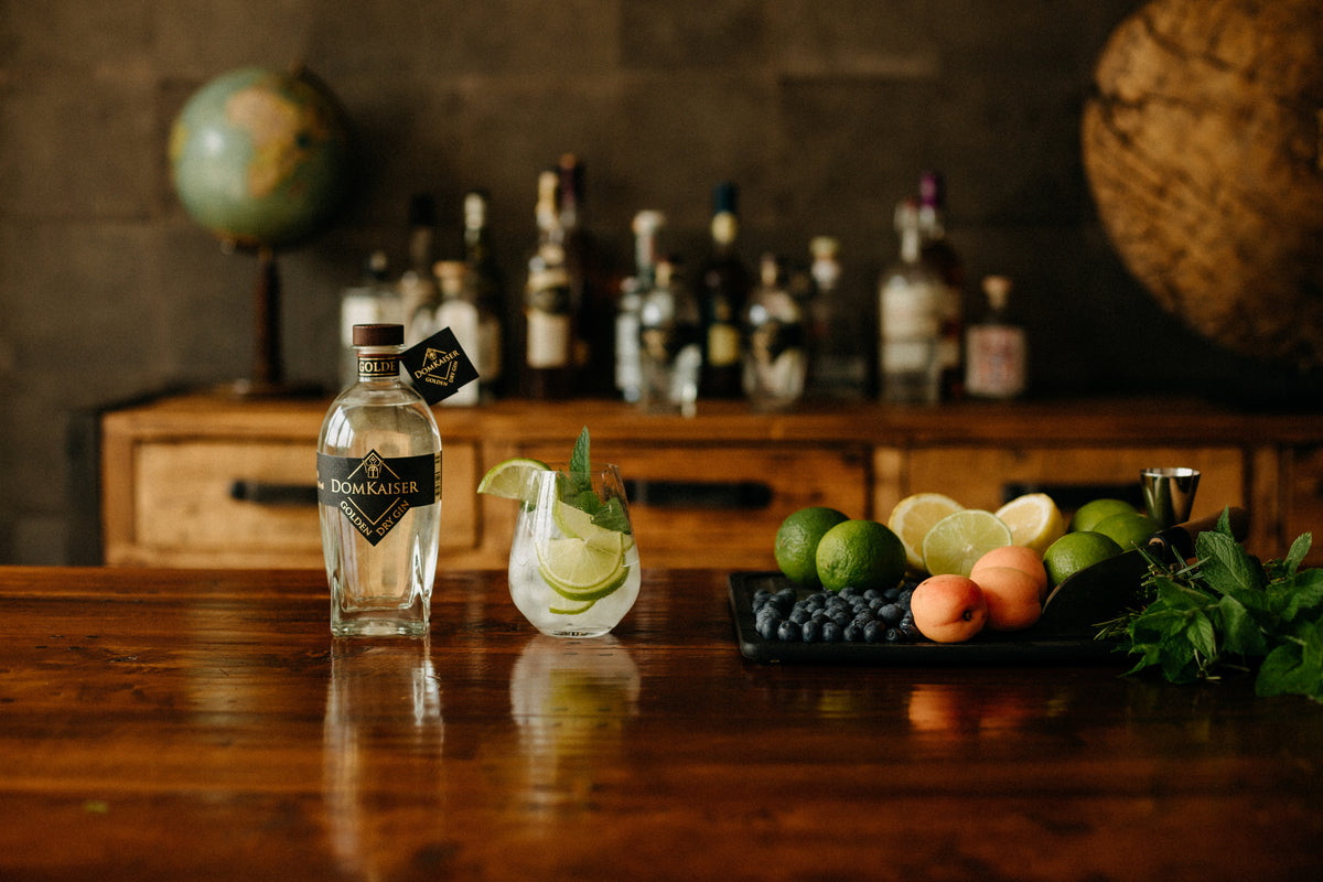 Domkaiser Golden Dry Gin Flasche mit Glas neben Obstschale auf einem massivem Holztisch in stilvollen Zimmer